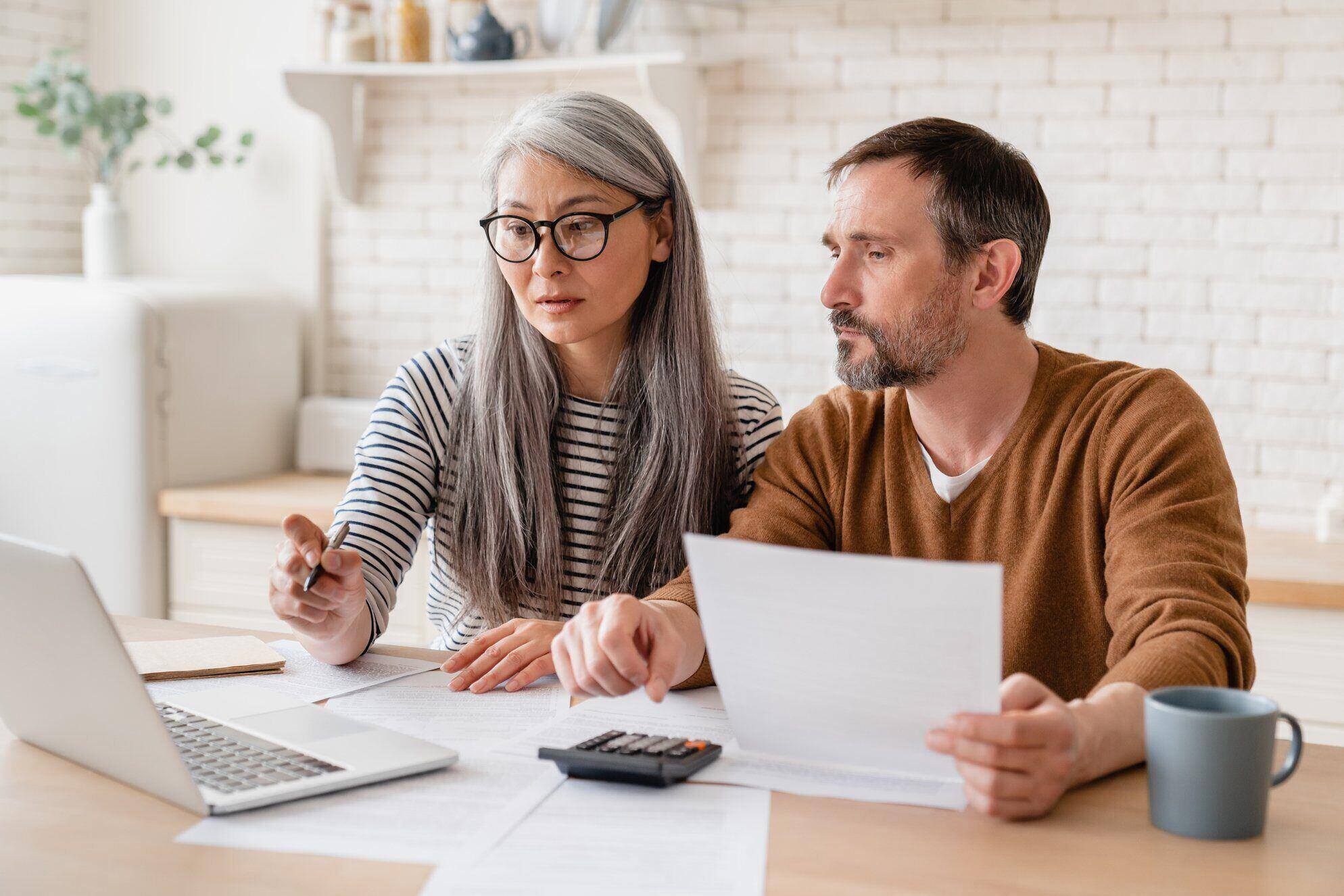 Mature couple looking at documents and a laptop determining the costs and benefits of purchasing a home warranty