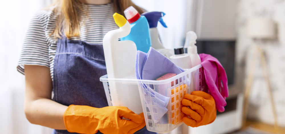 a woman holding a basket of spring cleaning supplies